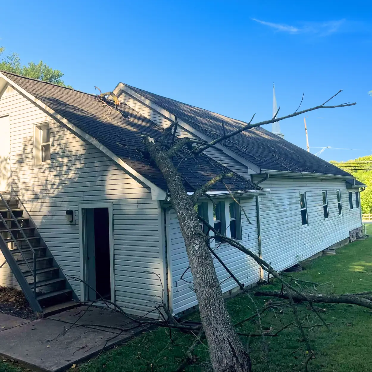 Large fallen tree branch resting on the shingle roof of a church after a storm.