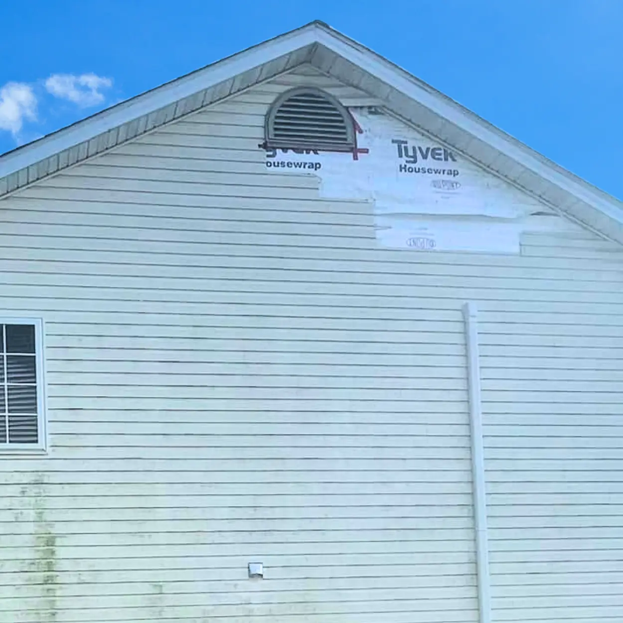 Two-story home with a section of vinyl siding missing after storm damage.