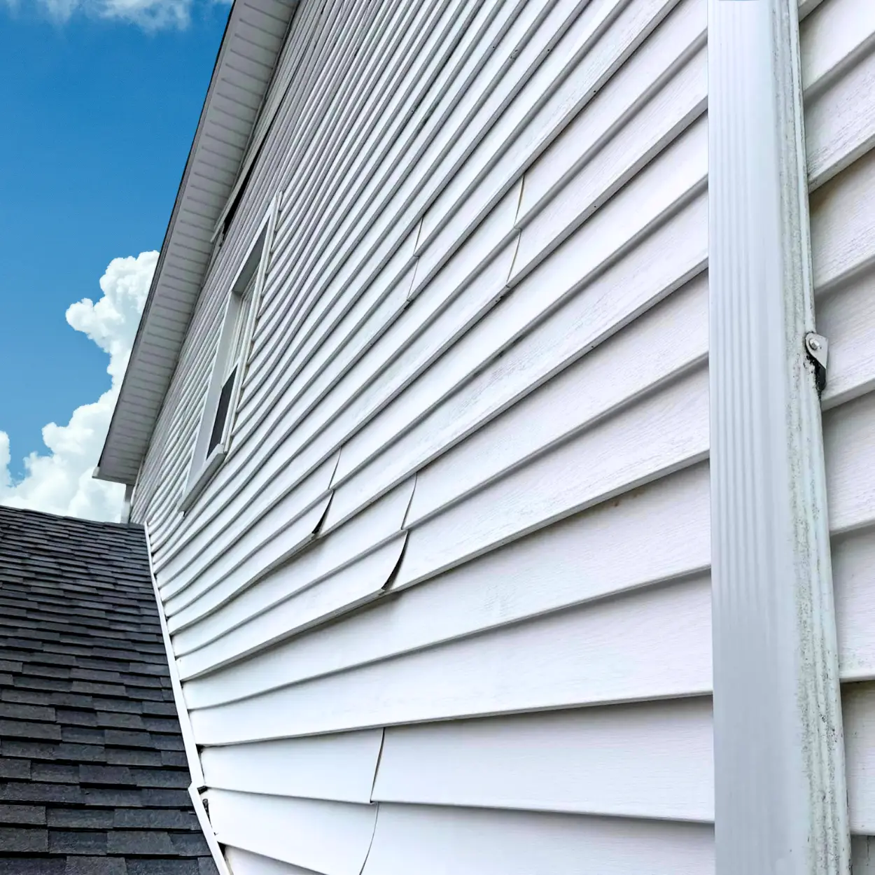 Warped and buckled white vinyl siding on the exterior of a residential home.