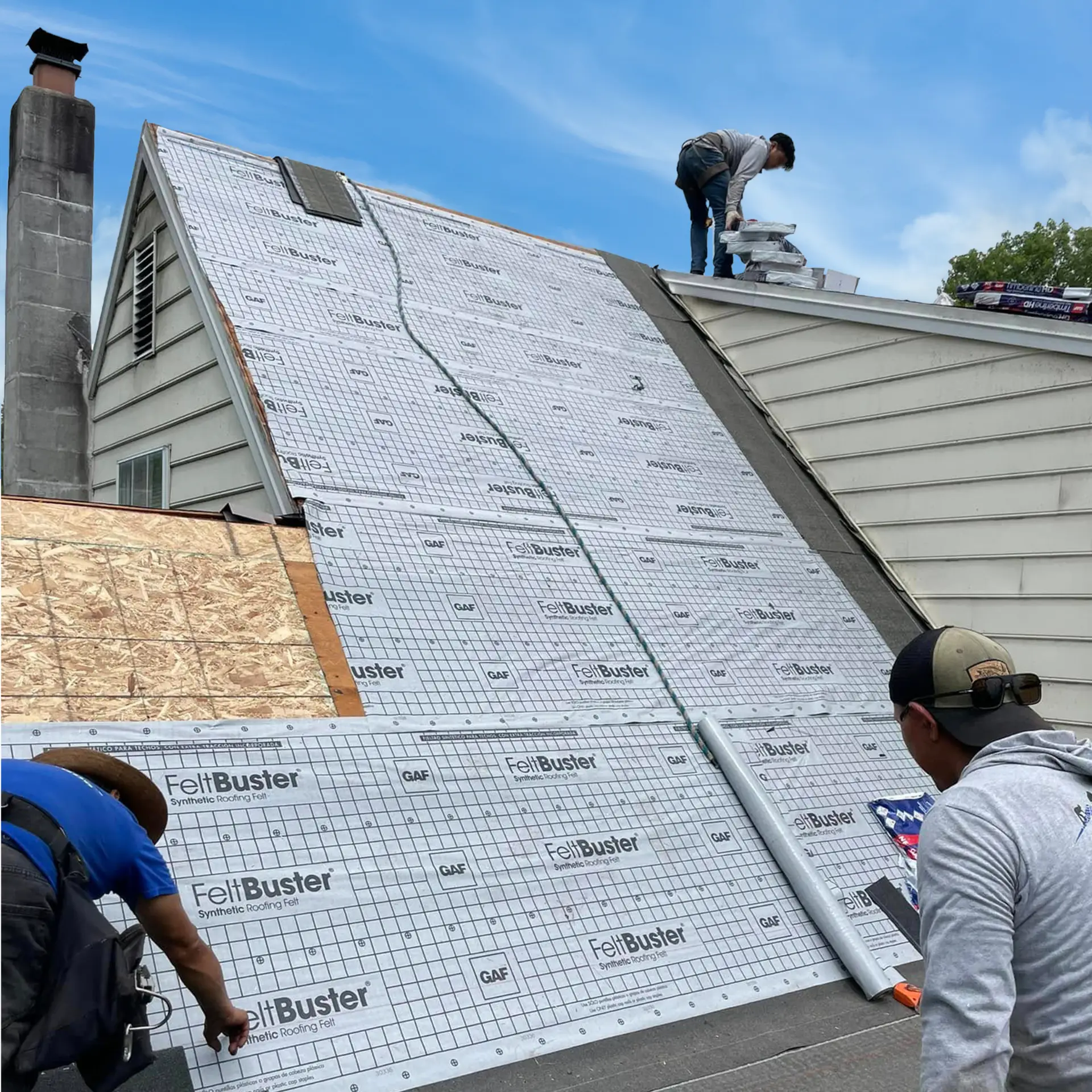 Roofing crew installing a new asphalt shingle roof with exposed roof decking and underlayment visible.