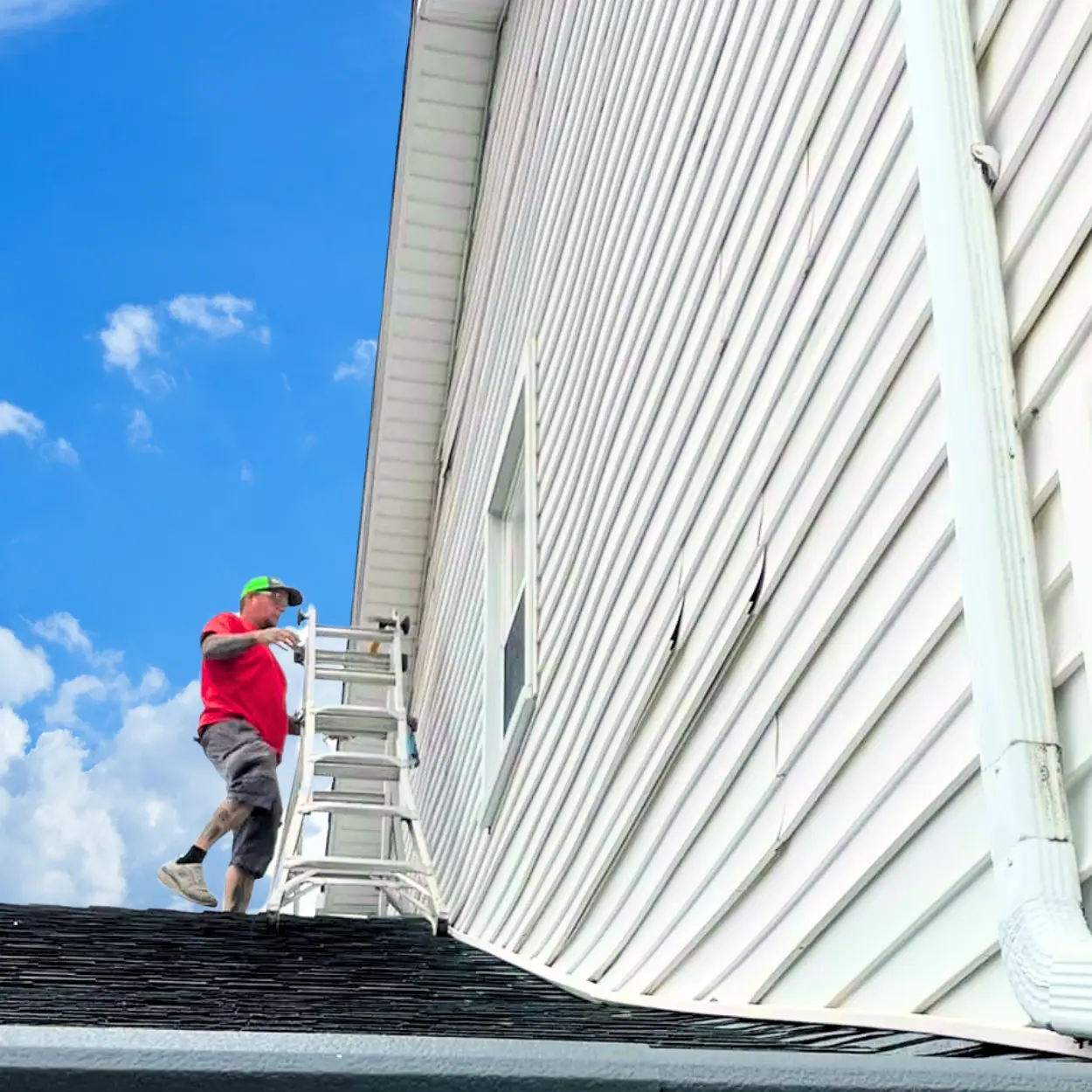 Roofing and siding professional inspecting the exterior vinyl siding of a two-story home from a ladder.