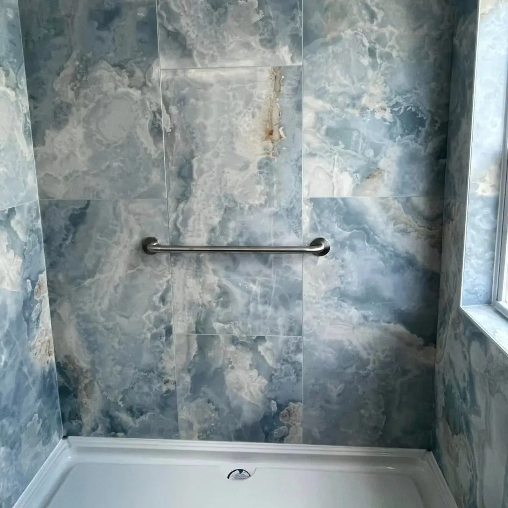 A shower showing installation of large blue wall tiles around the shower and window area