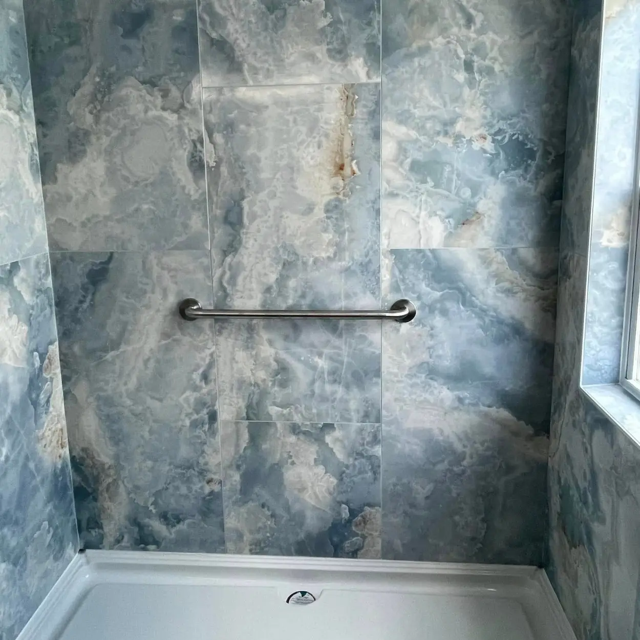 A shower showing installation of large blue wall tiles around the shower and window area