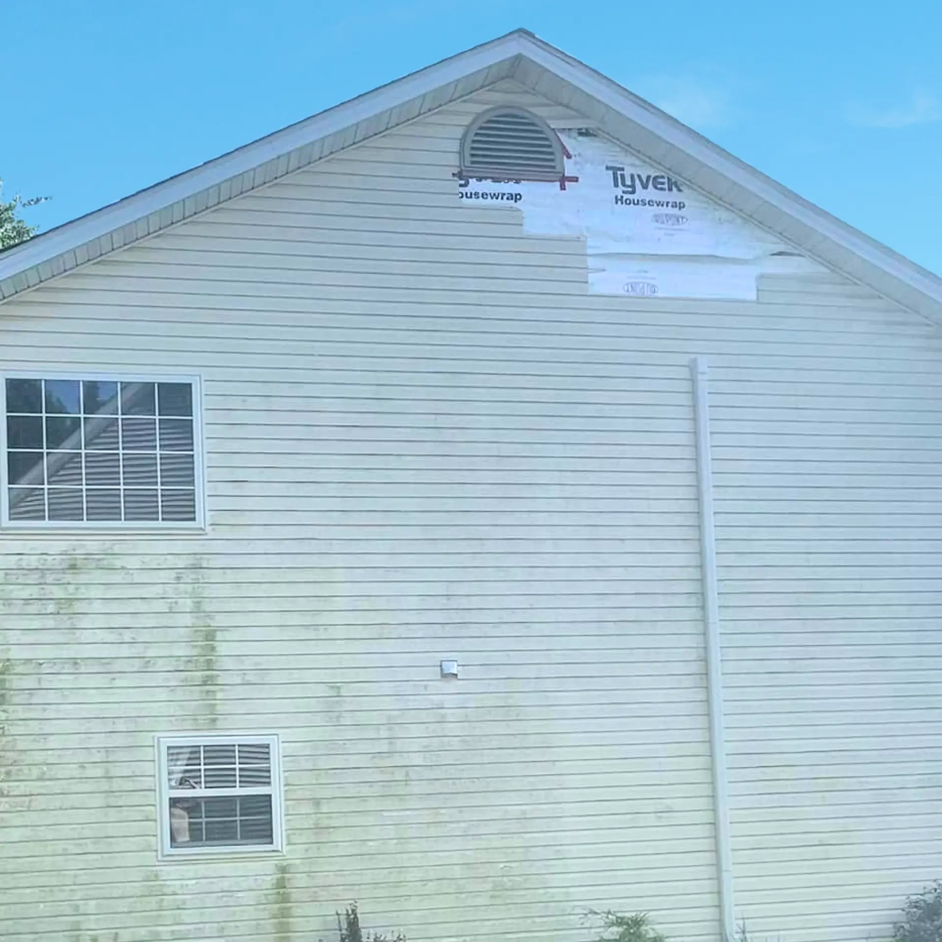 Two-story home with a section of vinyl siding missing after storm damage.