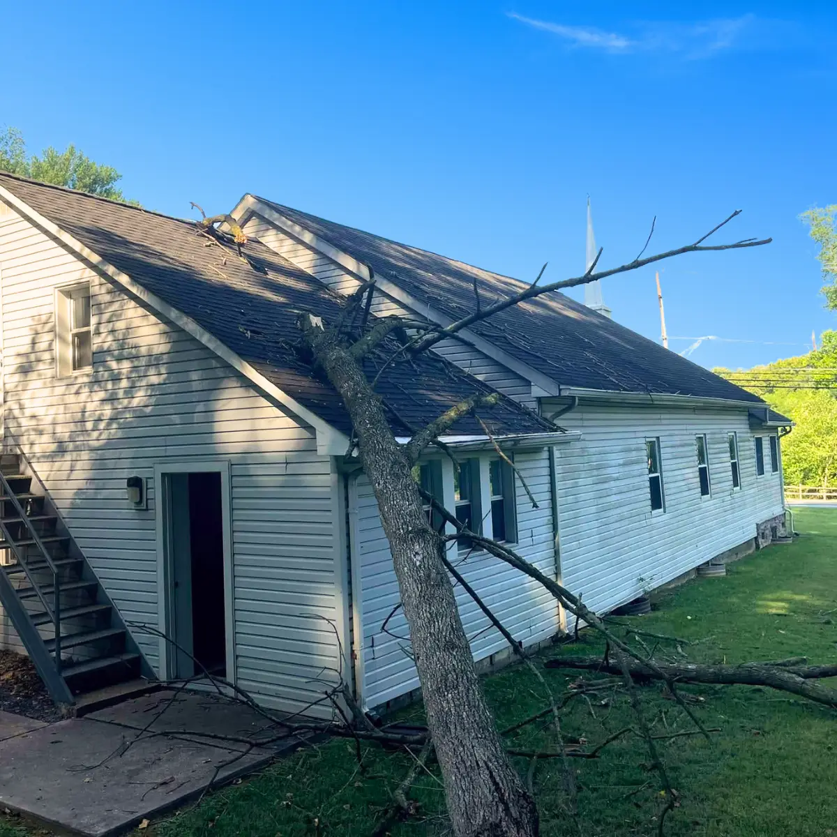 Large fallen tree branch resting on the shingle roof of a church after a storm.