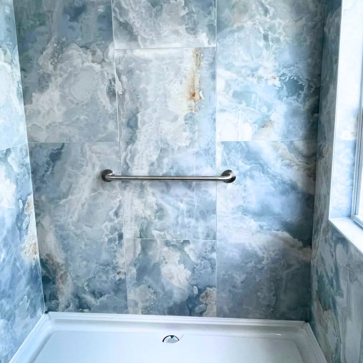 A shower showing installation of large blue wall tiles around the shower and window area